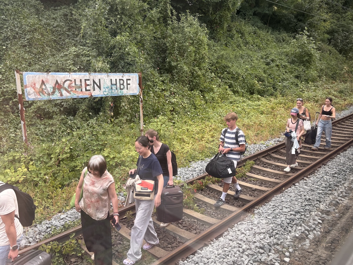 people walking down train tracks next to a out of service train carrying all their belongings